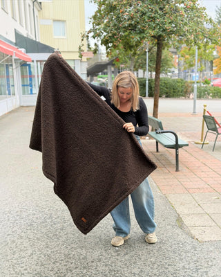 Kvinna som håller upp en mörkbrun, fluffig CAZO hundfäll från Hundinspiration utomhus.