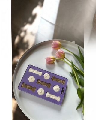 Hundinspiration Fiboo Iceboo glassform i lila TPE-material fylld med hundgodis på ett vitt bord med tulpaner