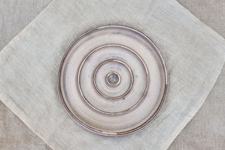 Hundinspiration handgjord keramisk slow feed-matskål i linnevit glasyr med spiralmönster på en linneduk.
